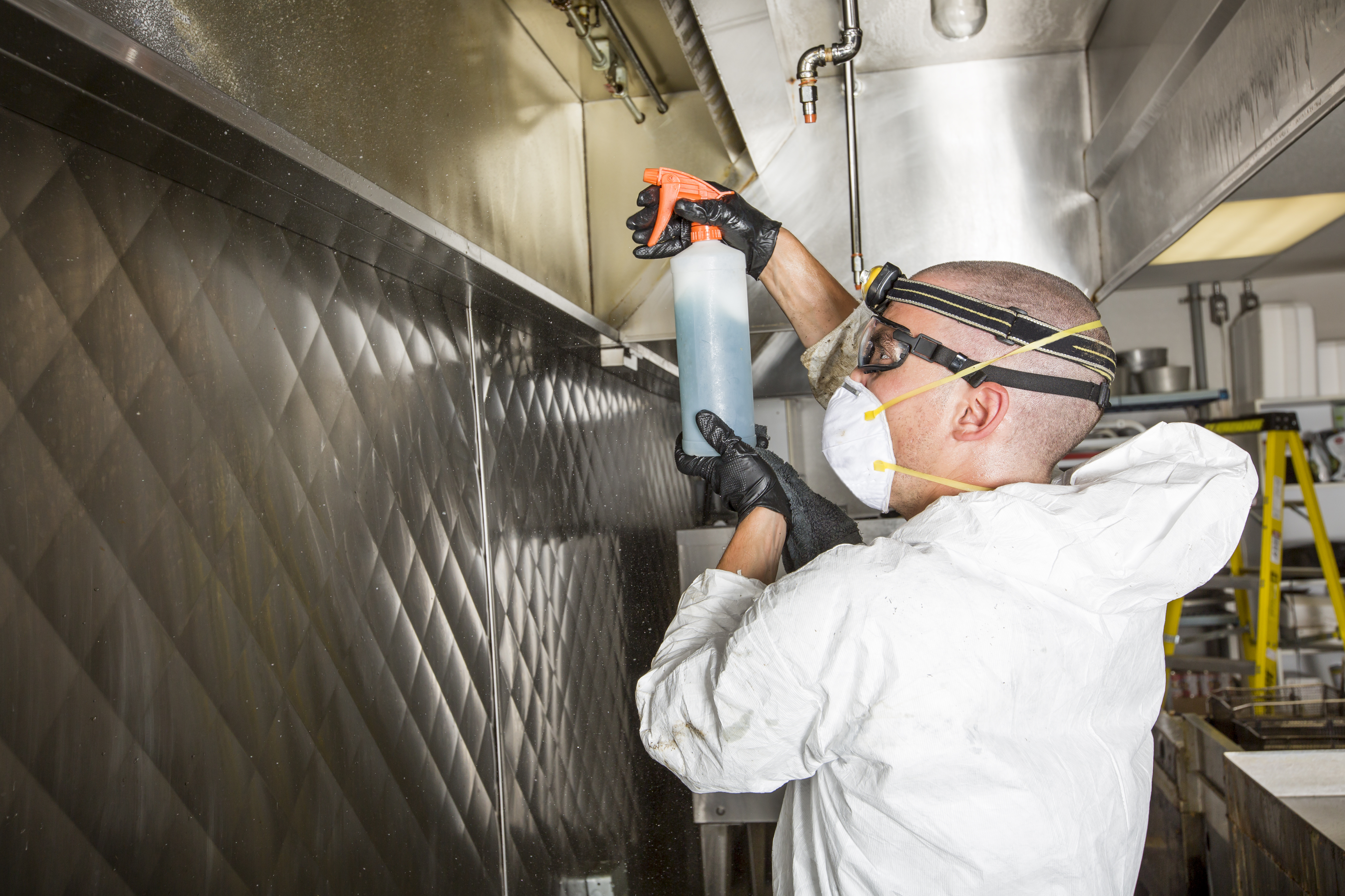 Ontario Hood Cleaning technician applying food-safe degreaser to the interior plenum of a commercial kitchen hood before scraping it back to bare stainless steel