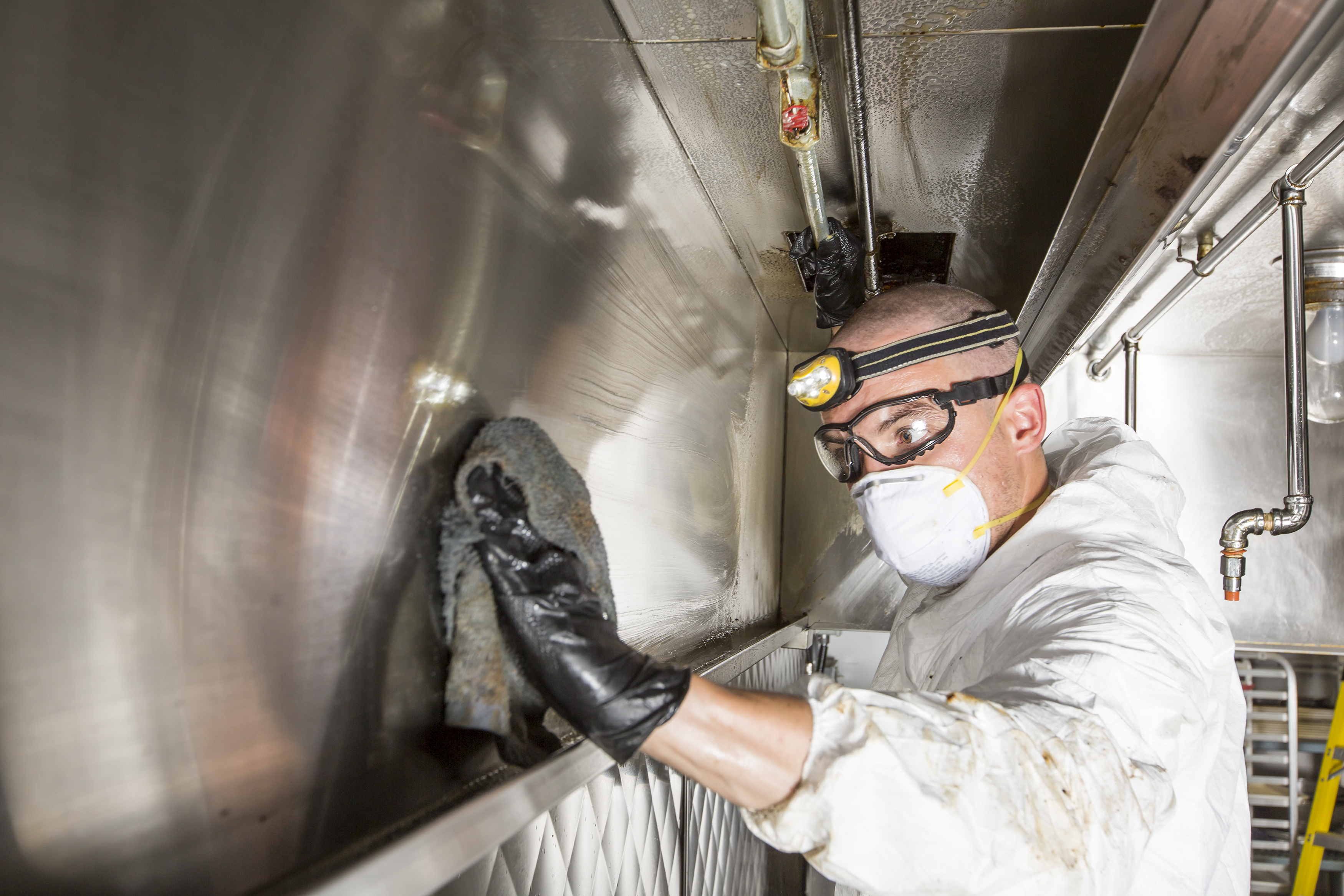 Ontario Hood Cleaning technician buffing the exterior of a stainless-steel commercial kitchen hood canopy during an overnight after-hours service visit