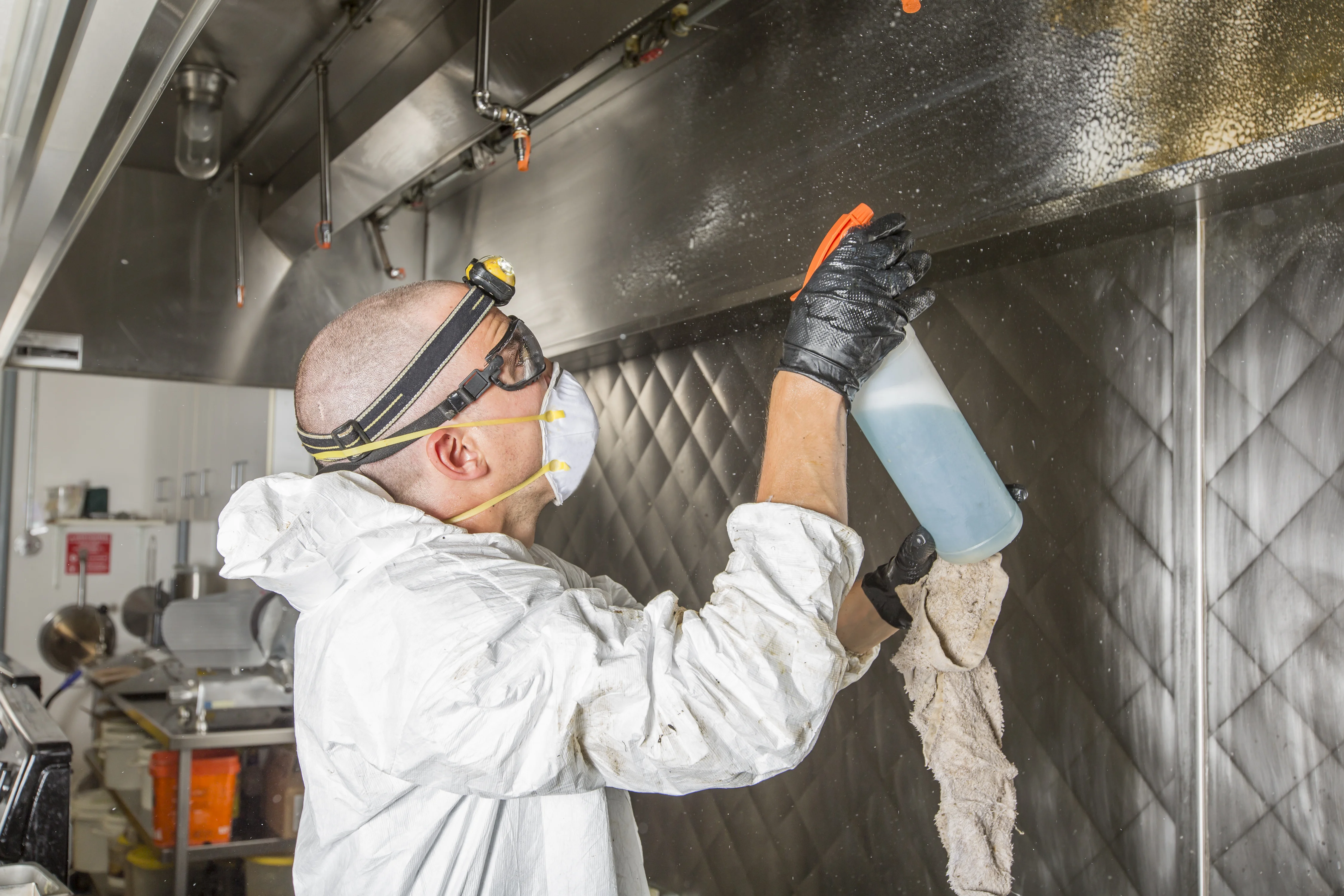 Technician scrubbing the interior of a commercial kitchen hood with full PPE