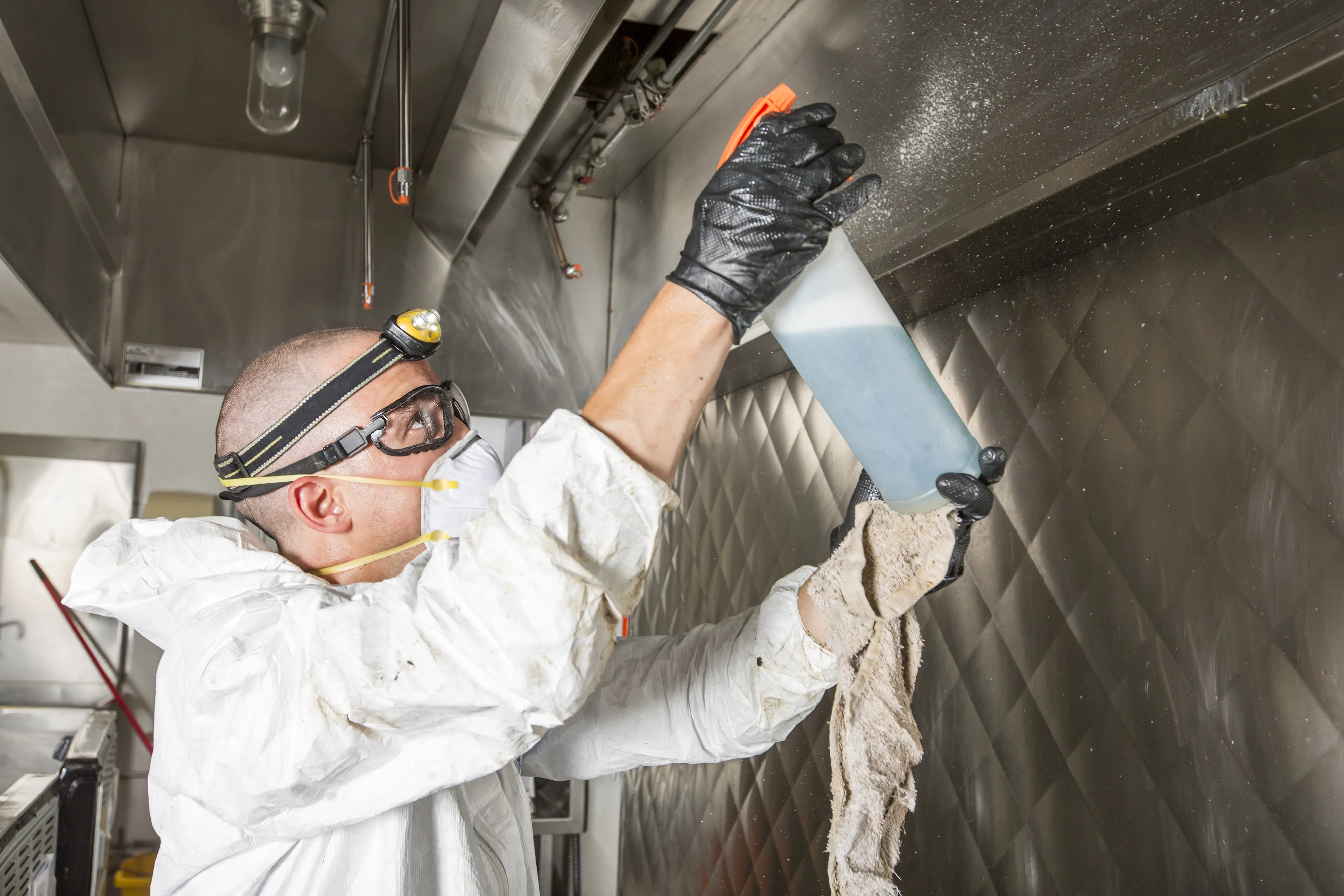 Commercial kitchen exhaust cleaner applying degreaser to a stainless hood baffle in an Ontario restaurant