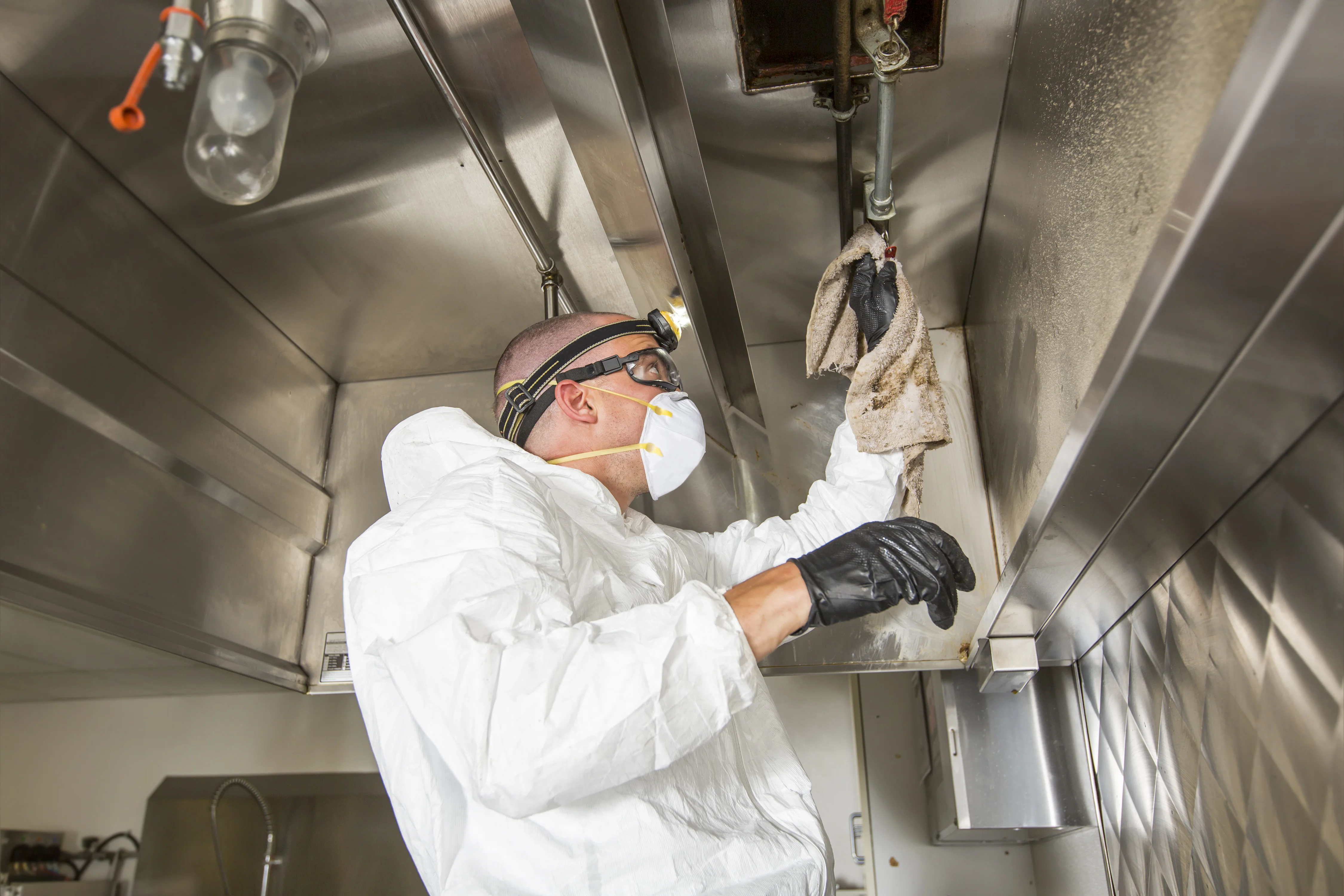 Ontario Hood Cleaning technician hand-wiping the interior of an opened horizontal grease duct above a commercial kitchen cook line during an NFPA 96 service visit